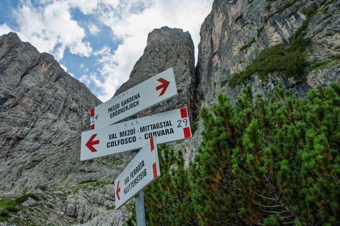 Wegweiser zum Klettersteig Pisciadù. Im Hintergrund die Hängebrücke, für die Kletterer, welche den Pisciadù Klettersteig hoch klettern.