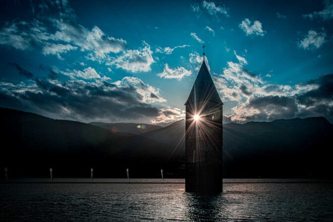 Sonnenuntergang am Reschensee. Die letzten Strahlen fallen durch den Glockenstuhl des versunkenen Kirchturms.