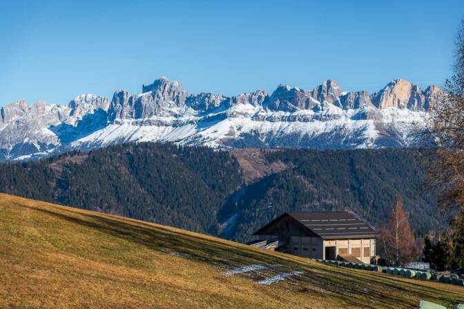 Bauernhof am Panoramaweg unter dem St.-Helena-Kirchlein in Deutschnofen. Im Hintergrund der angezuckerte Rosengarten.